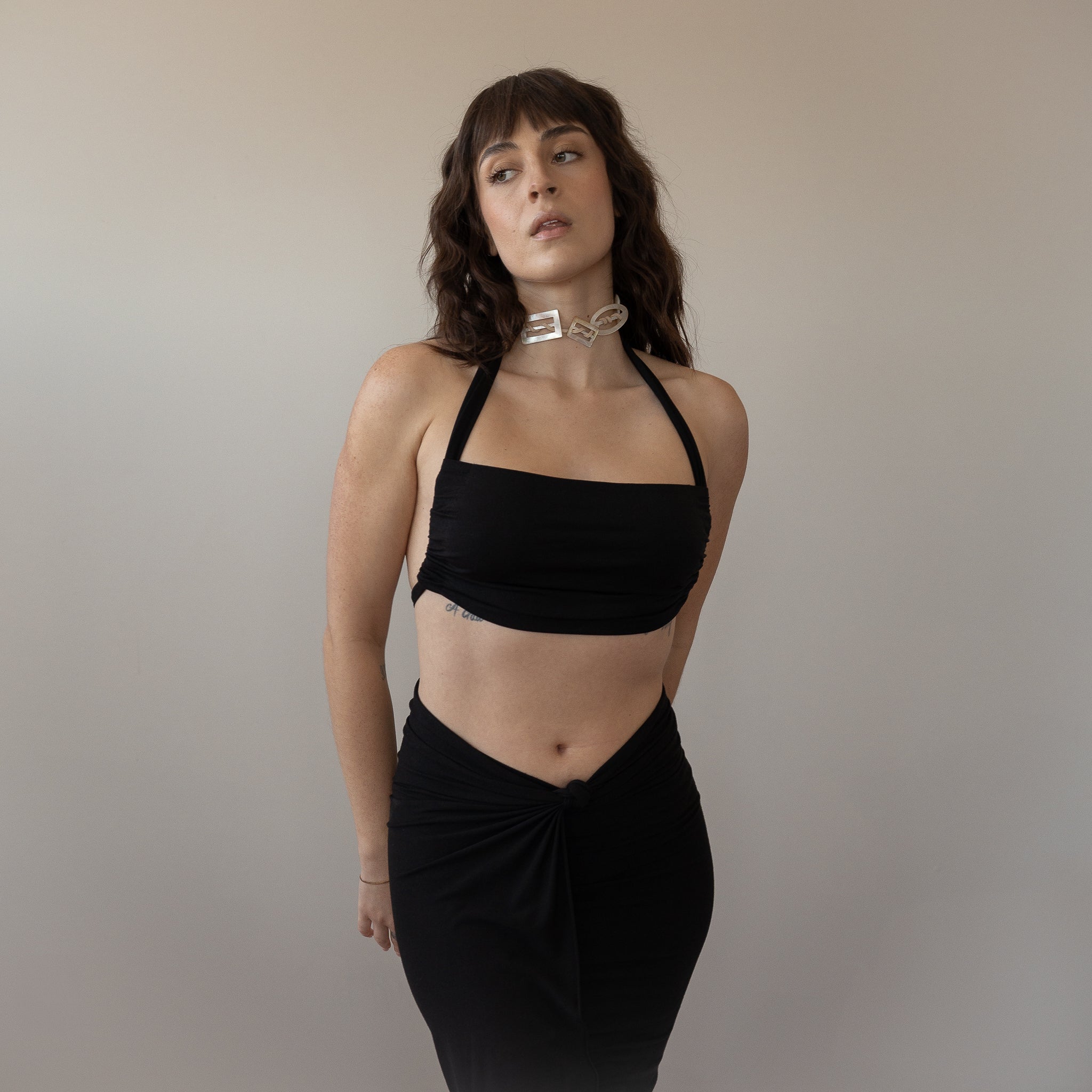 Woman wearing a black halter top and black skirt against a plain background